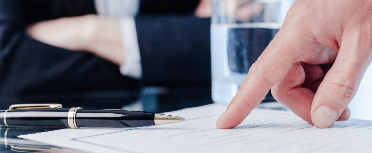 person pointing to a contract with another person behind sitting with crossed arms in the background