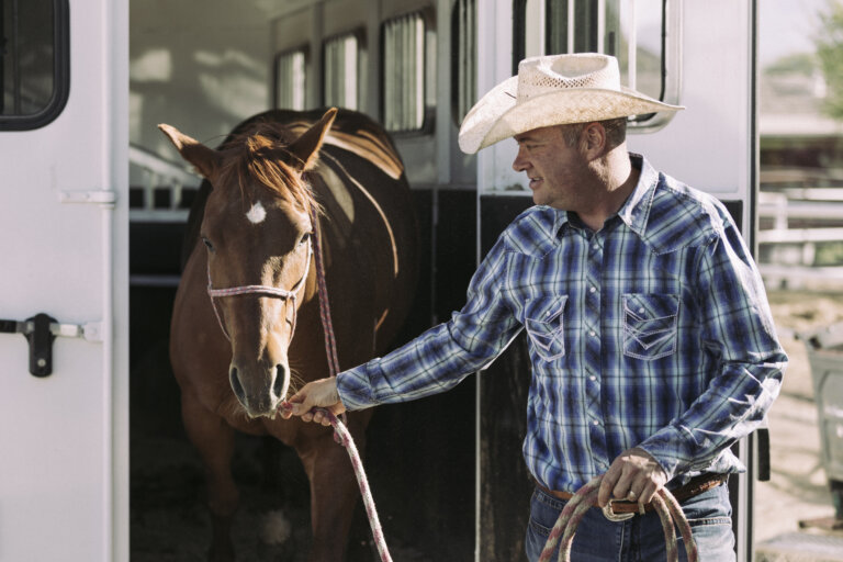 Man in a cowboy hat leading a brown horse out of a trailer