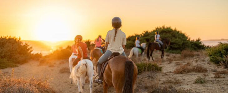 group of young riders on horseback heading towards the beach