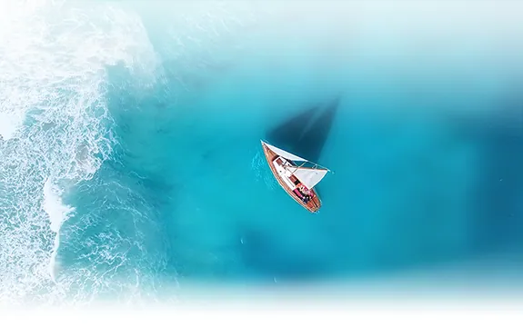 Aerial view of a small sailboat navigating through clear turquoise waters